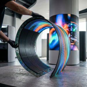 Flexible LED display panel being bent into a curved shape showing vibrant colors on a cylindrical pillar installation